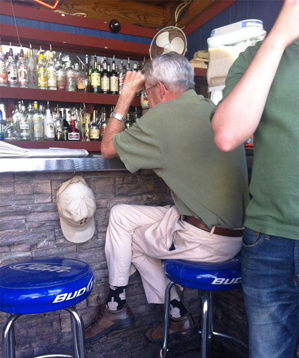 a man sitting at a bar with two stools in front of him and bottles on the wall behind him