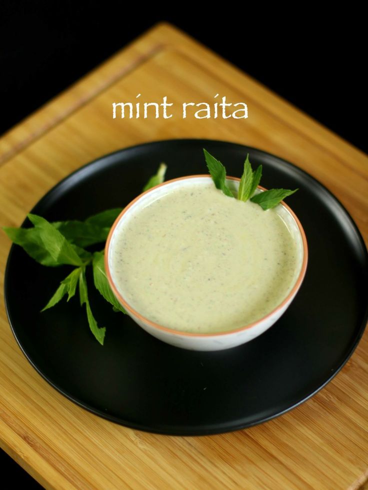 a black plate topped with a small bowl filled with green liquid and garnished with leaves