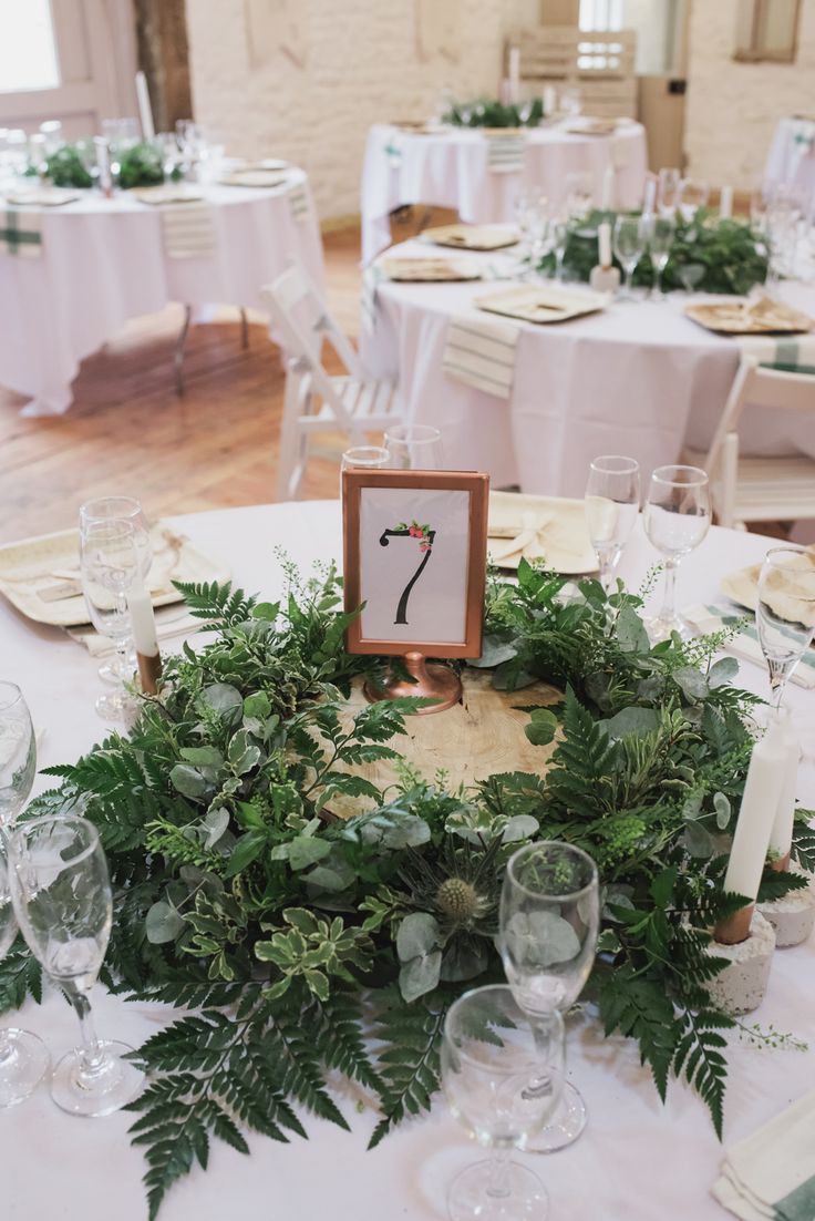 the table is set up with white linens and greenery