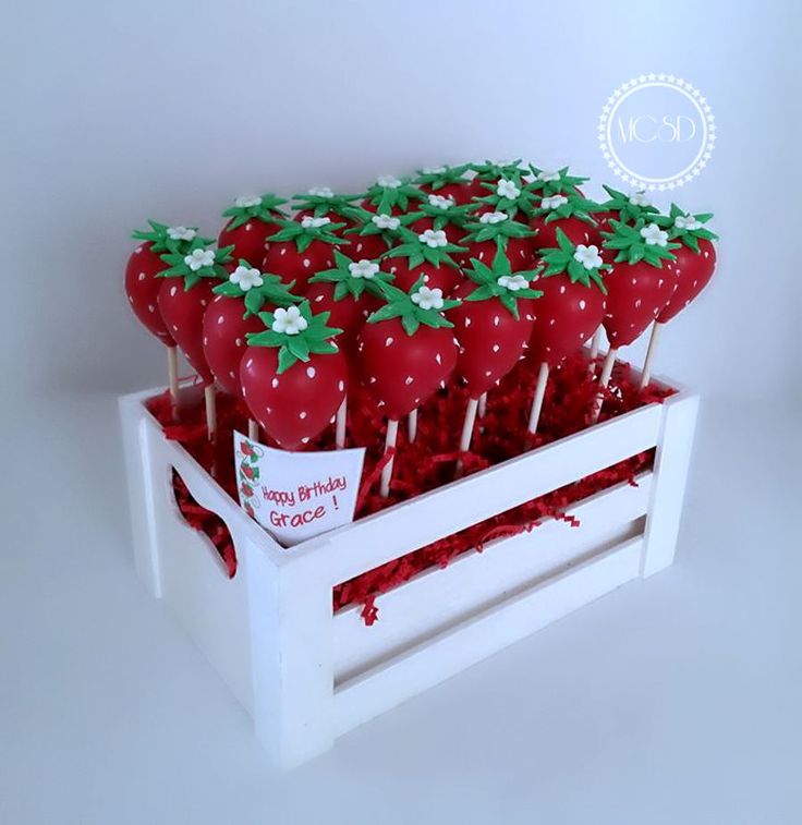 strawberries are arranged on sticks in a white box with red and green decorations,