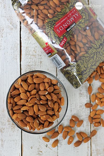 almonds in a glass bowl next to a bag of almonds on a white wooden table