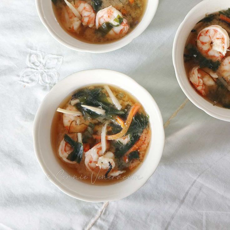 three bowls of soup with shrimp and spinach in them on a white tablecloth