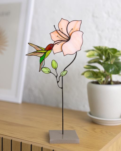 a pink flower sitting on top of a wooden table next to a potted plant