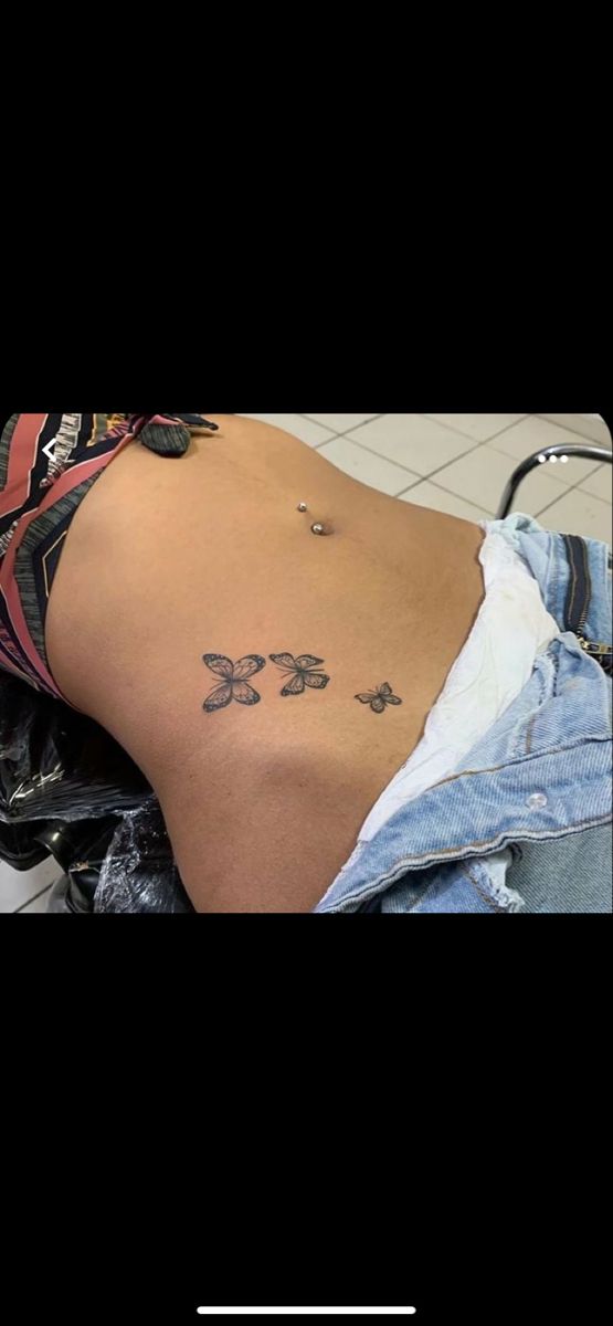 the back of a woman's stomach with small tattoos on her left side, and an arrow in the middle