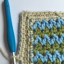 a crocheted square with a blue handled knitting needle