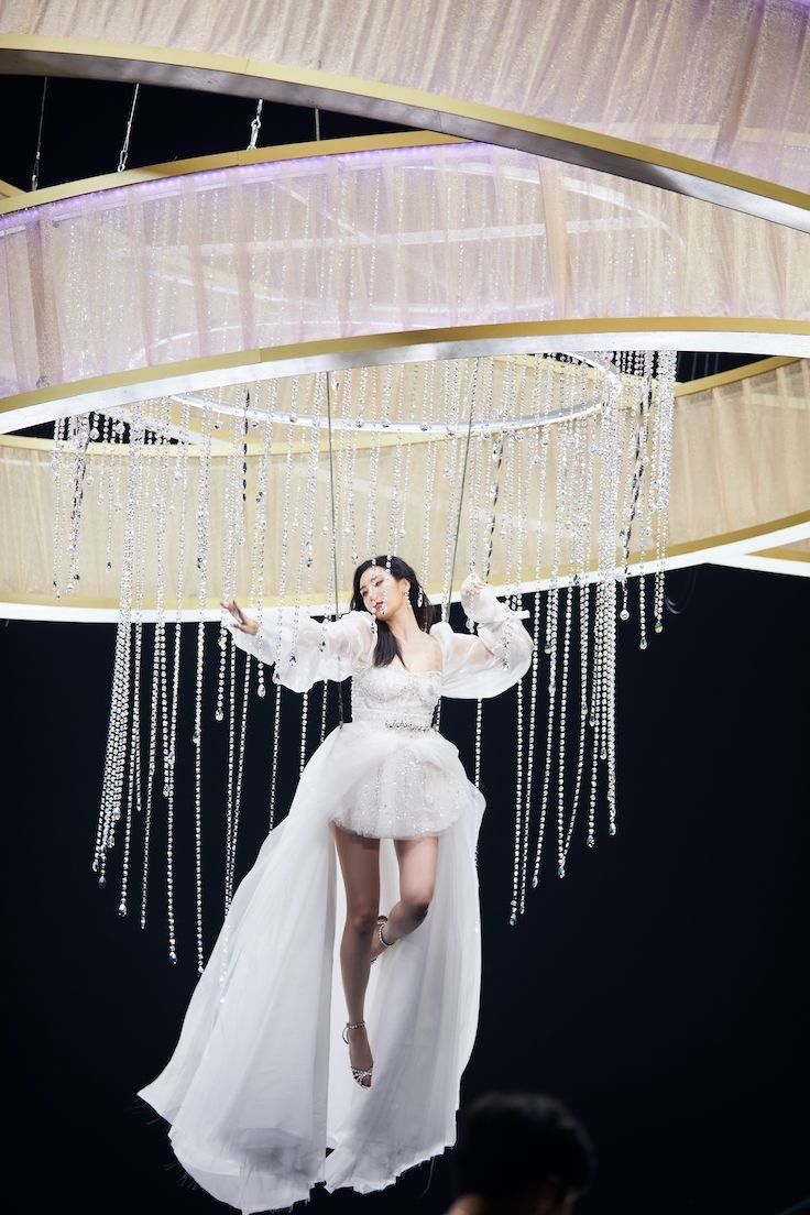 a woman in a white dress is suspended from a chandelier