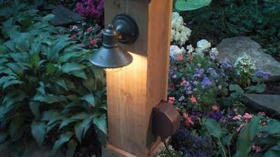 a wooden post with a light on it in the middle of some plants and flowers