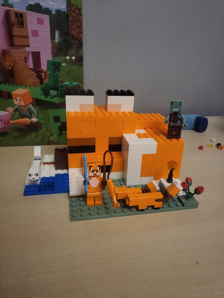 an orange and white lego house on top of a wooden table next to a poster