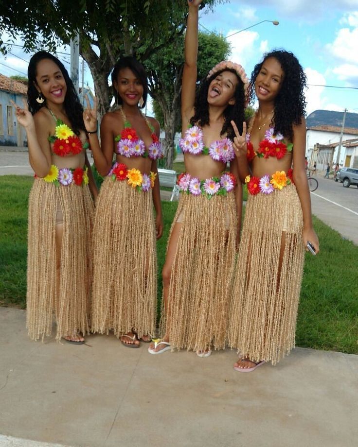 three women in grass skirts and flower leis are standing on the sidewalk with their hands up