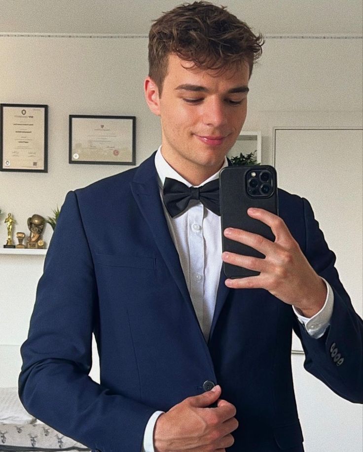 a man in a tuxedo taking a selfie with his cell phone while wearing a bow tie