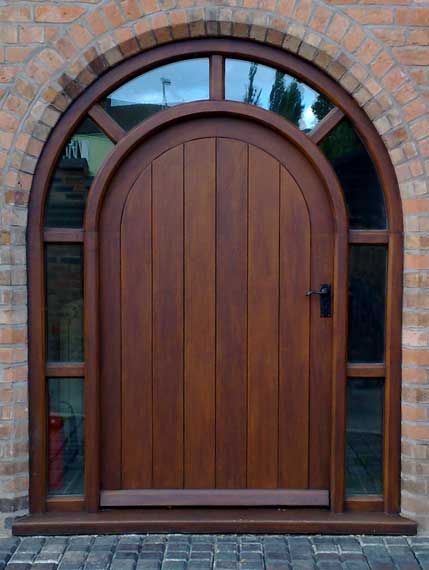 a wooden door with arched glass in front of a brick wall and stone flooring