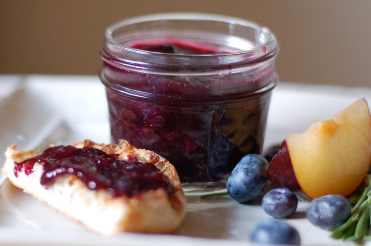 a glass jar filled with blueberry sauce next to some fruit on a white plate