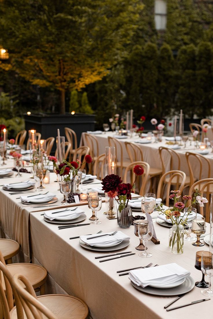 a long table is set with white plates and place settings for an outdoor dinner party