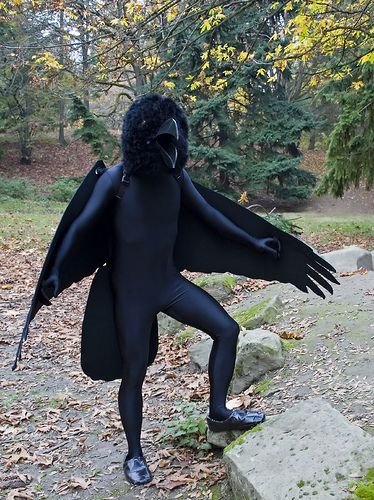 a man dressed in black is standing on some rocks with his arms outstretched and legs spread out