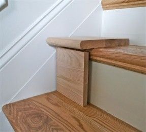 the corner of a wooden stair case in a room with white walls and wood flooring