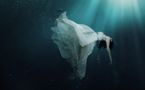 a woman floating in the water wearing a white dress