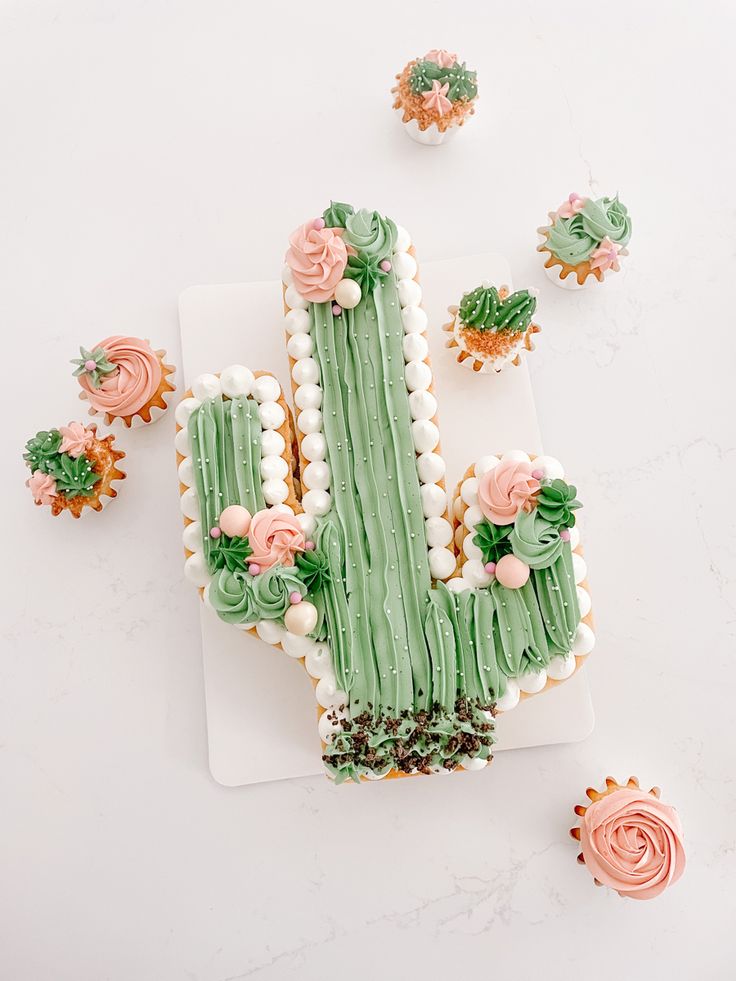 a cake shaped like a cactus on top of a white plate next to cupcakes