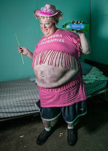 a woman in a pink shirt and hat standing next to a bed with green walls