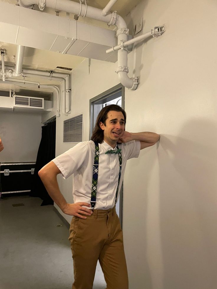 a man standing next to a wall with his hands on his hips wearing a tie