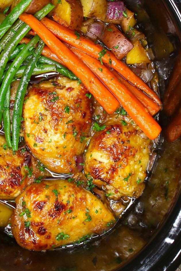 a crock pot filled with chicken, potatoes and green beans next to carrots