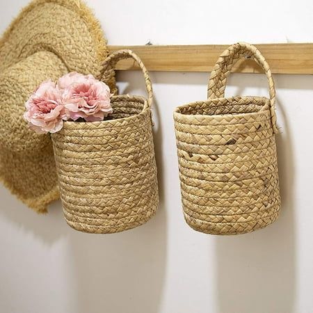 two baskets are hanging on the wall with flowers in them and one has a pink flower