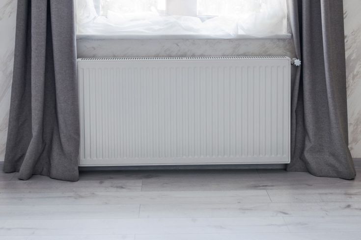 a white radiator sitting next to a window with curtains on top of it