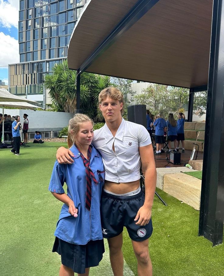 a man and woman standing next to each other in front of a building with grass