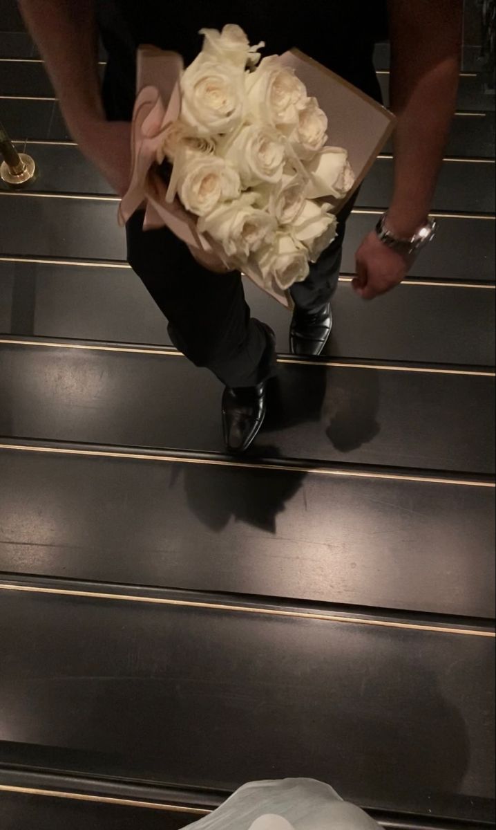 a man holding a bouquet of white roses on top of some escalator steps