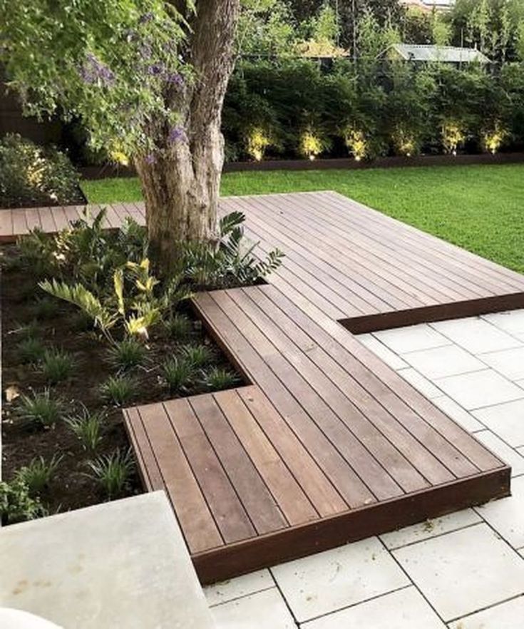 a wooden deck in the middle of a garden with trees and plants around it,