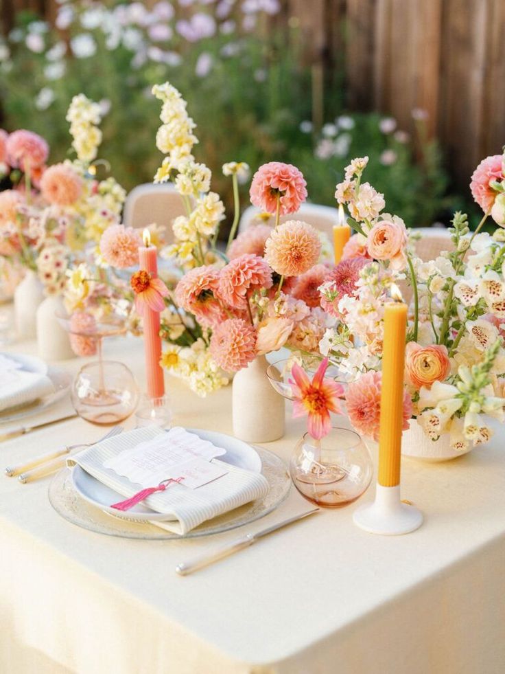 the table is set with white and pink flowers in vases, candles, and napkins