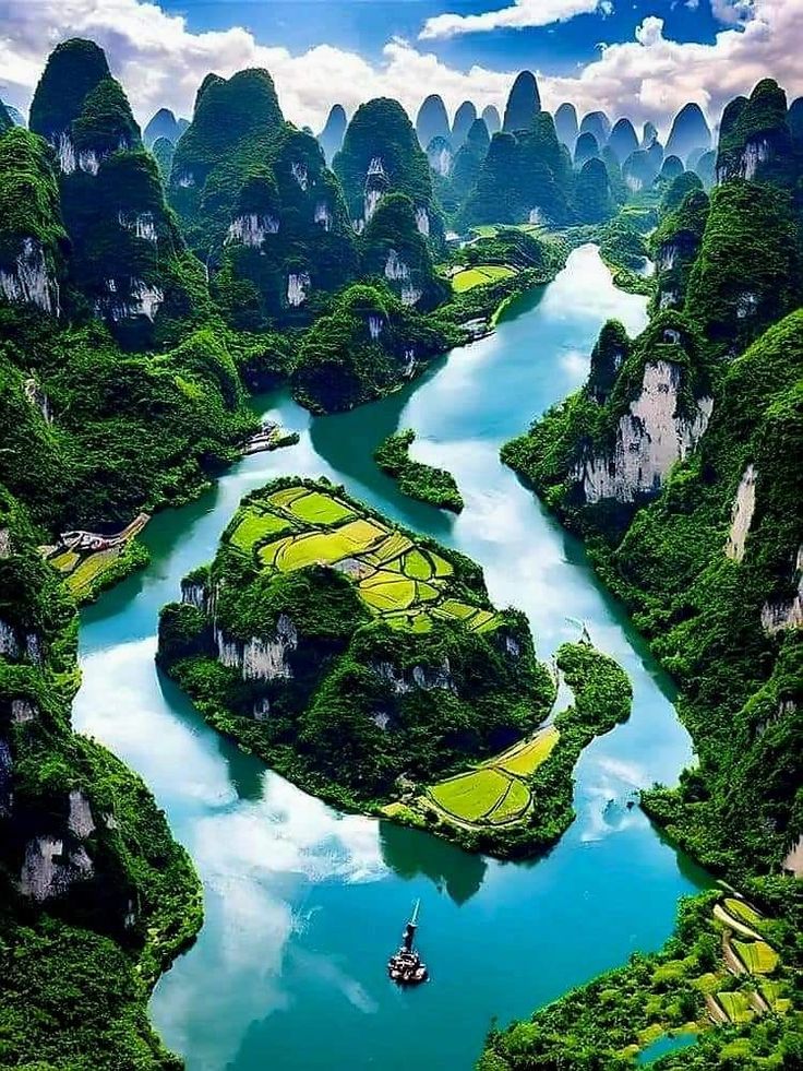 an aerial view of a river surrounded by lush green mountains and greenery, with a boat in the water