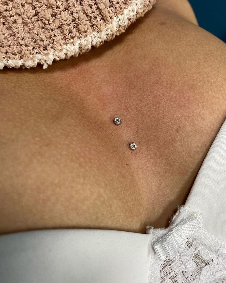 a close up of a woman's breast with two small diamond studs on it