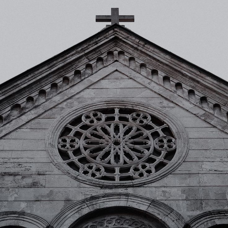 an old church with a cross above it and a window on the front wall that has a circular design