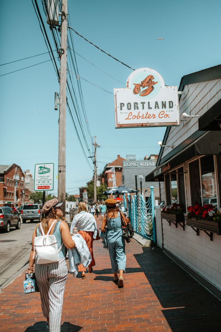 people walking down the sidewalk in front of a store with a sign that says portland lobster co