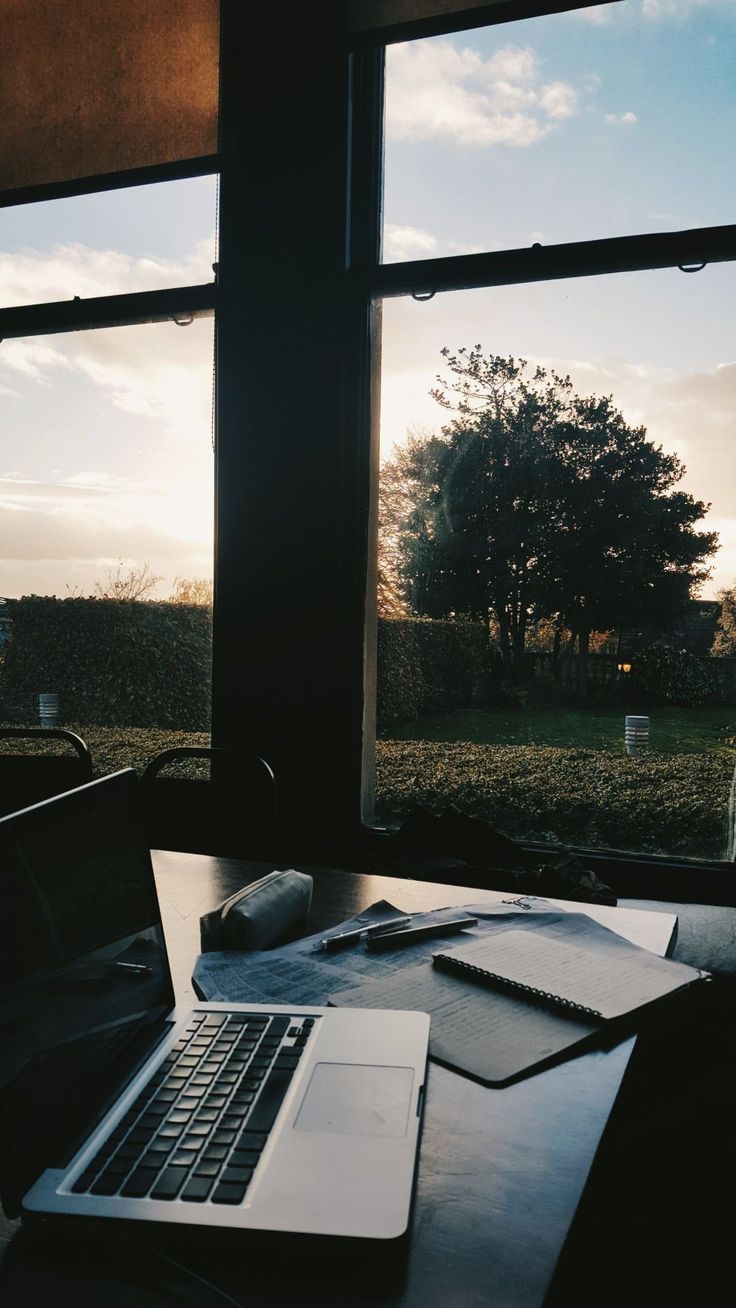 an open laptop computer sitting on top of a wooden table next to a large window