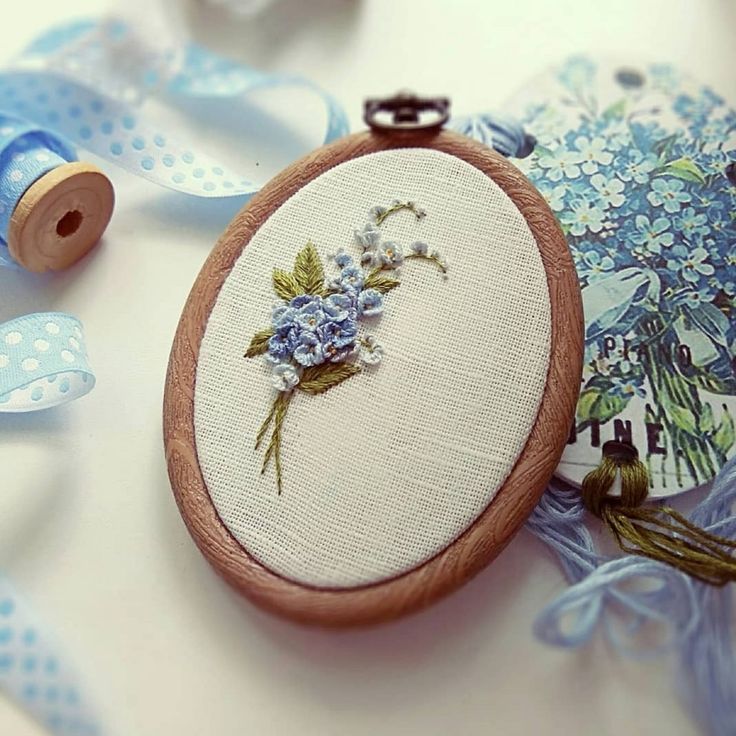 an embroidered flower on a wooden frame next to blue ribbon and spools of thread