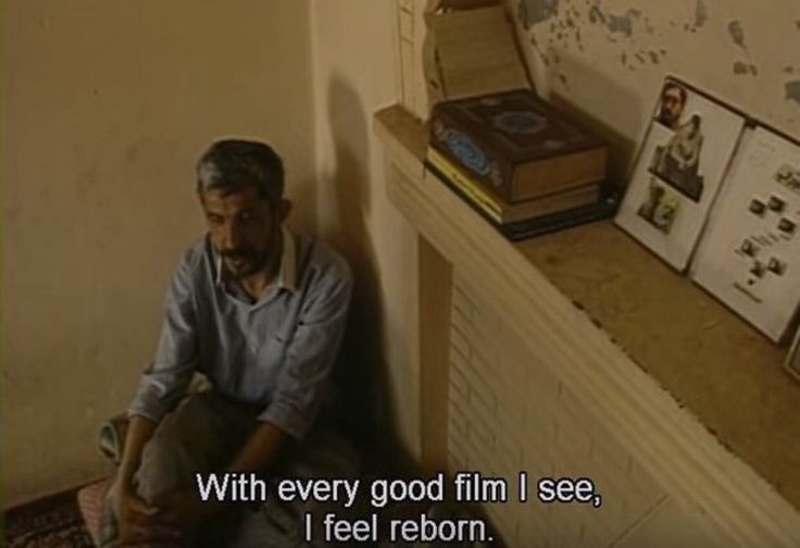 a man sitting on the floor in front of a wall with pictures and books behind him