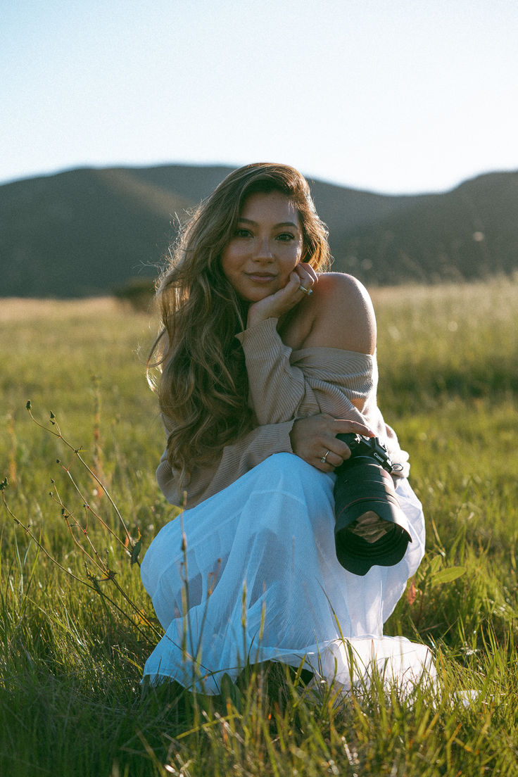 a beautiful young woman sitting on top of a lush green field