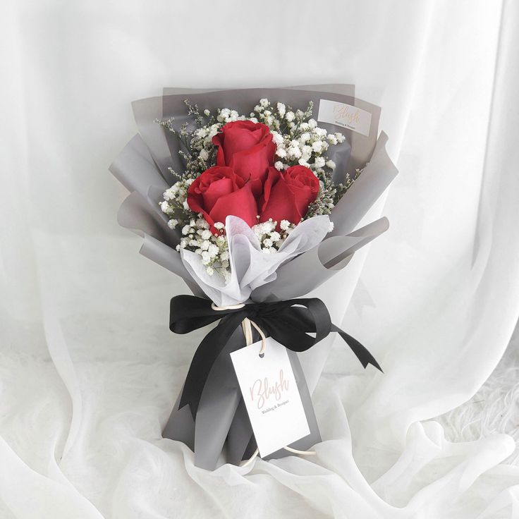 a bouquet of red roses and baby's breath wrapped in black ribbon on a white background