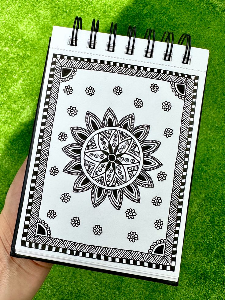 a hand holding a notebook with an intricate design on it