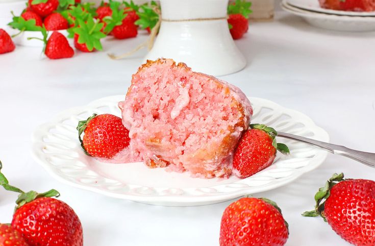 a piece of strawberry cake on a plate with strawberries around it and one slice missing