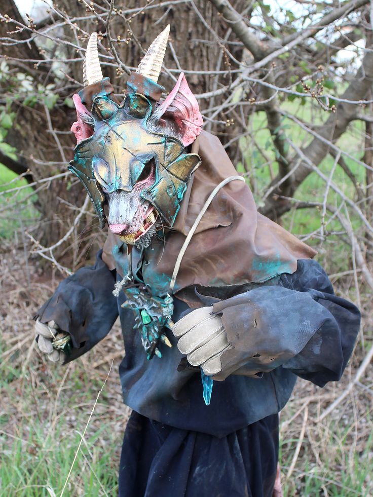 a costumed animal with horns and gloves on is holding something in his hands while standing next to a tree