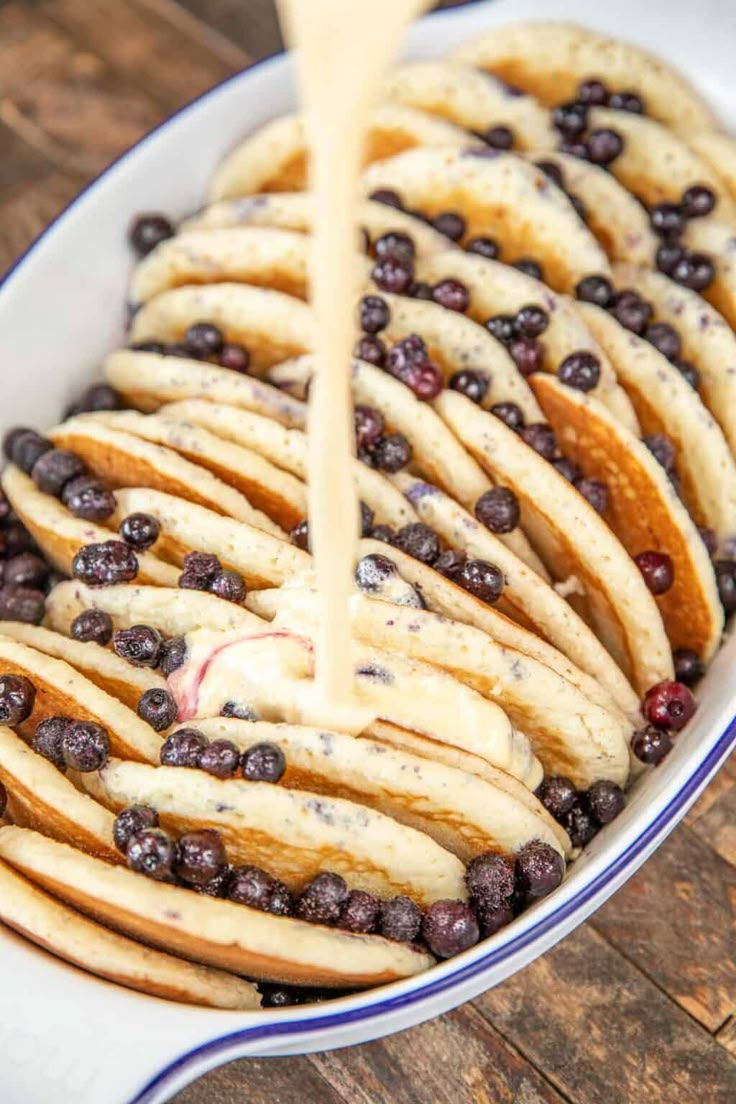 blueberries and cream cheesecake being drizzled with icing on a plate