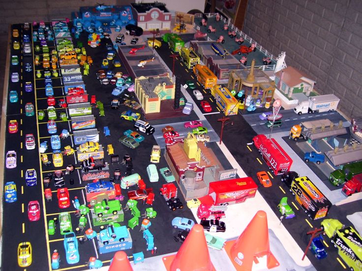 a table topped with lots of toy cars and trucks on top of a floor covered in traffic cones