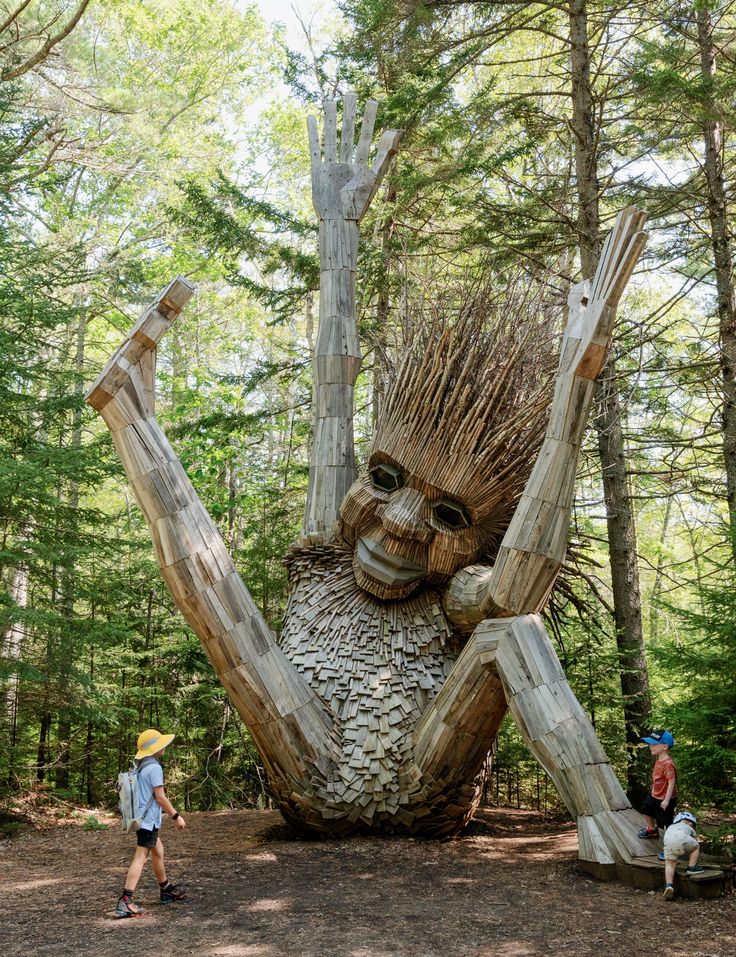 two people walking past a wooden sculpture in the woods