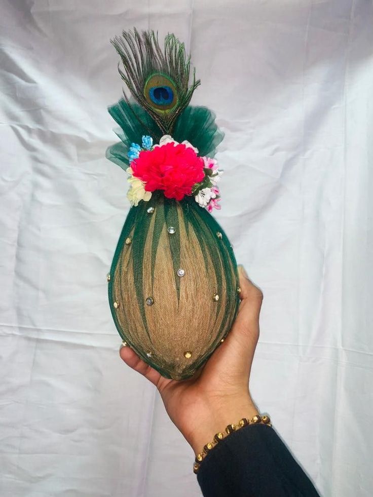 a person holding a vase with flowers and feathers on it's head, in front of a white backdrop