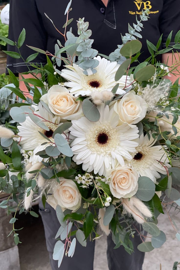 a man holding a bouquet of white flowers and greenery