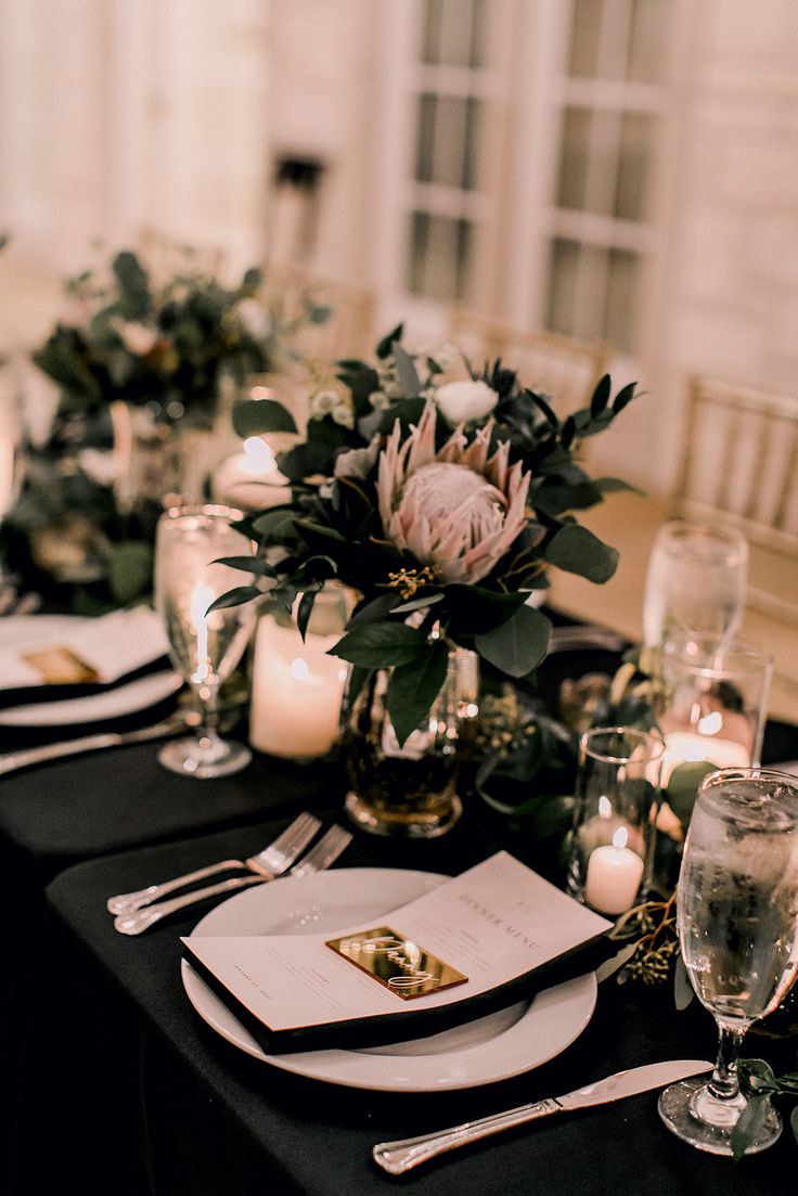 the table is set with black linens and white plates, silverware and candles