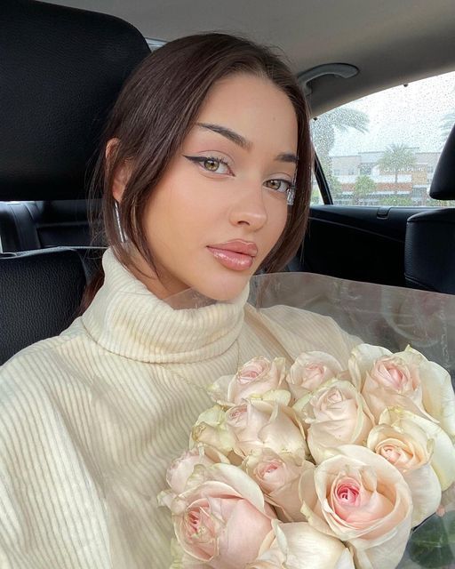 a woman sitting in the back seat of a car holding a bouquet of roses and looking at the camera