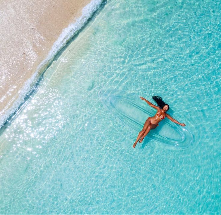 a woman floating in the ocean on top of a clear blue body of water with her arms outstretched